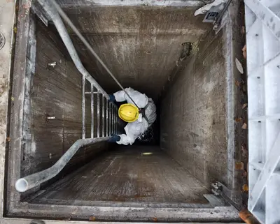 Mitarbeiter steigt den Kanalschacht hinunter
